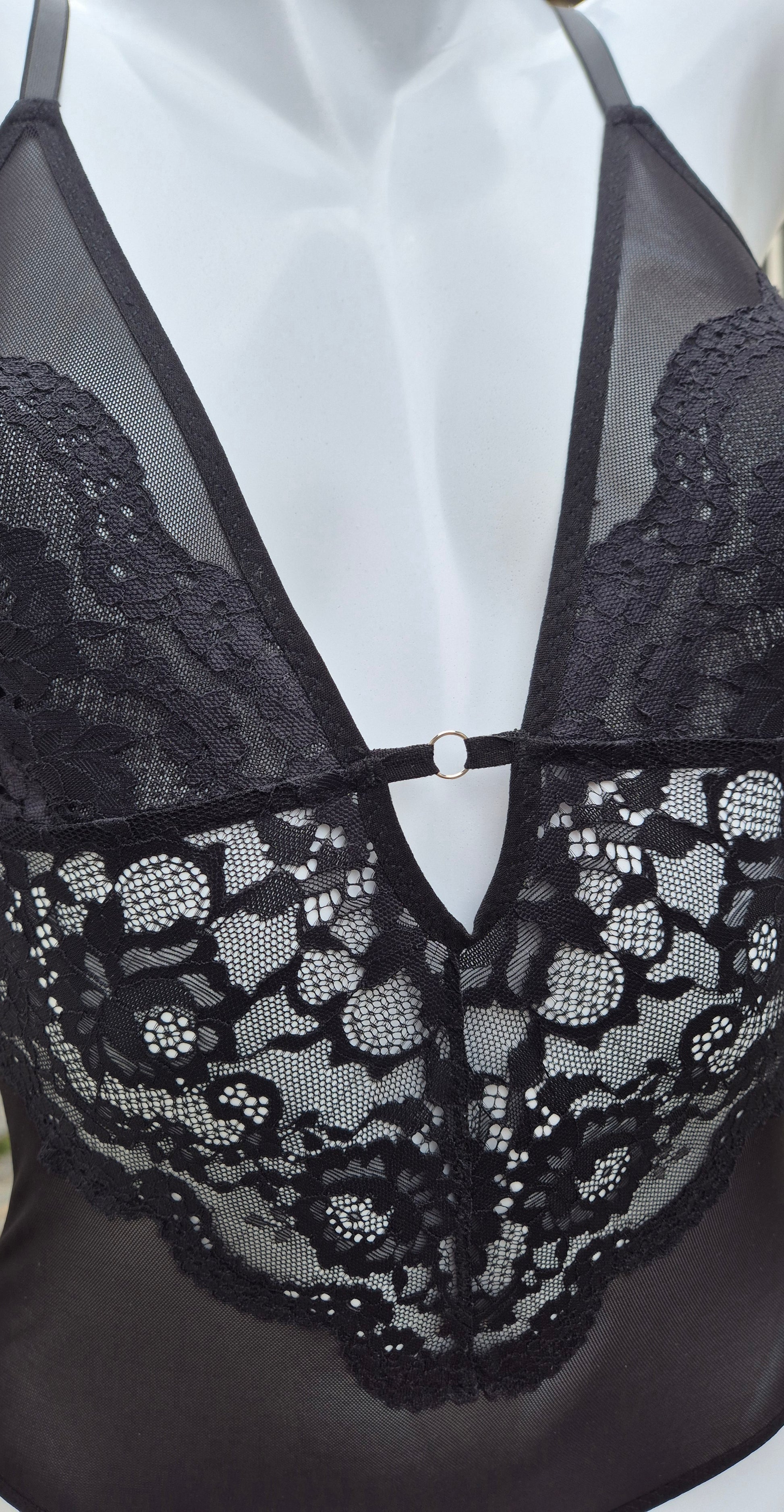 Body Luna preto em renda delicada com decote em V profundo, acabamento artesanal e detalhes femininos. Argola no decote na cor prata e plaquinha personalizada da marca em prata. 