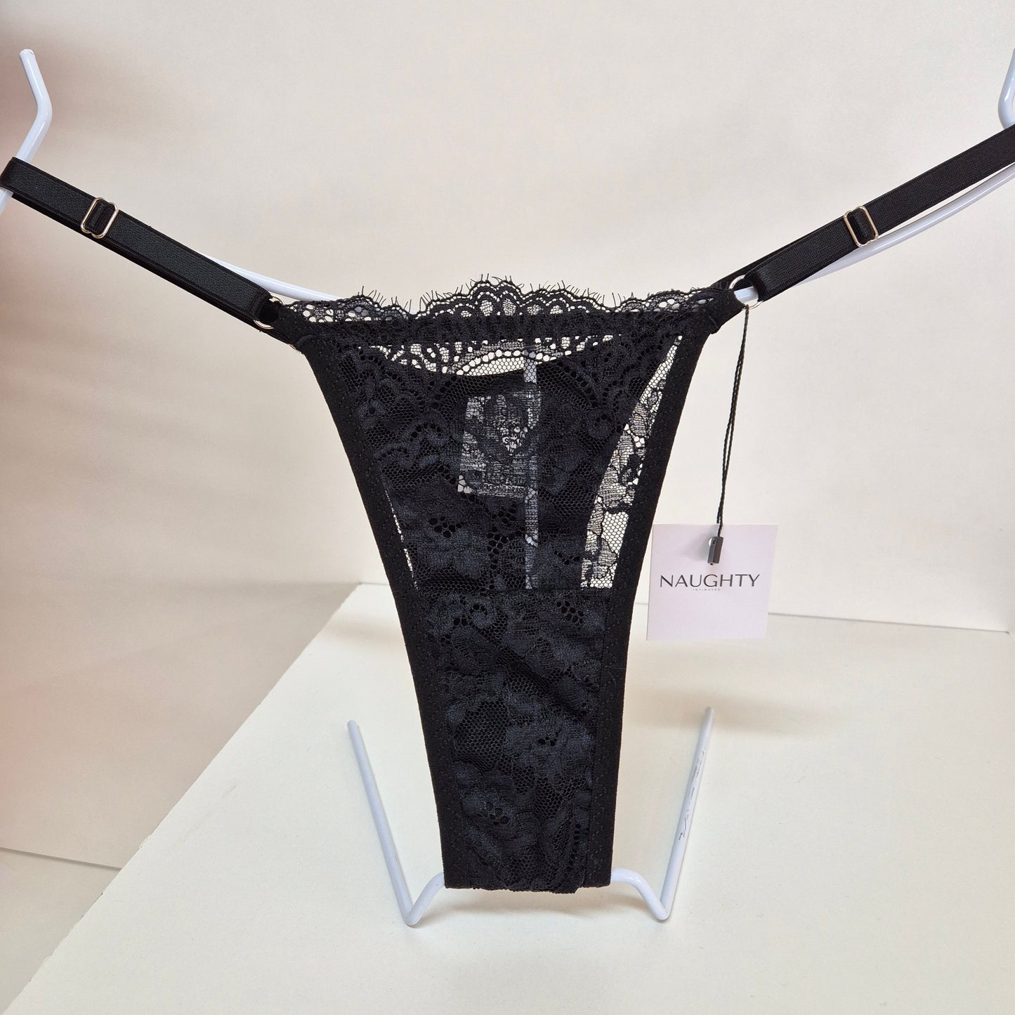 Calcinha string preta em renda macia e floral com alças finas ajustáveis e toque artesanal. Fio duplo em microfibra e plaquinha personalizada naughty na cor prata. 