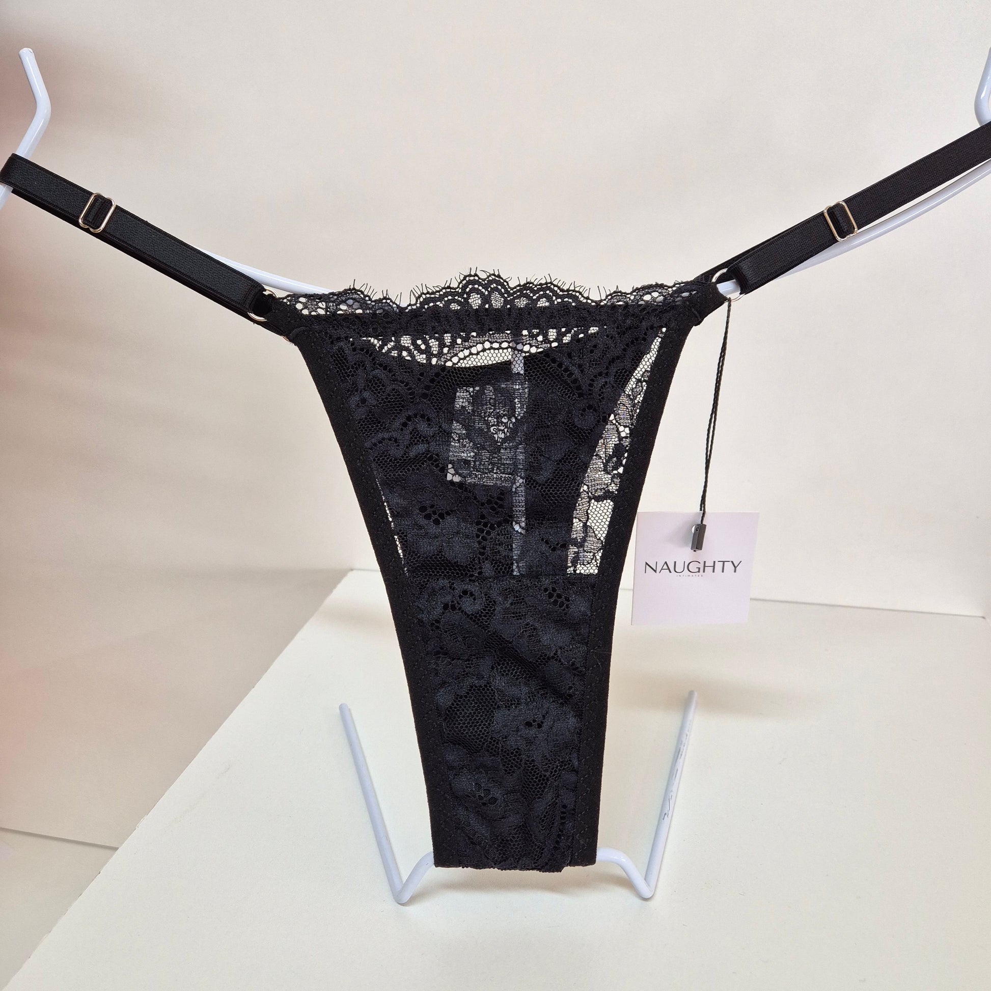 Calcinha string preta em renda macia e floral com alças finas ajustáveis e toque artesanal. Fio duplo em microfibra e plaquinha personalizada naughty na cor prata. 