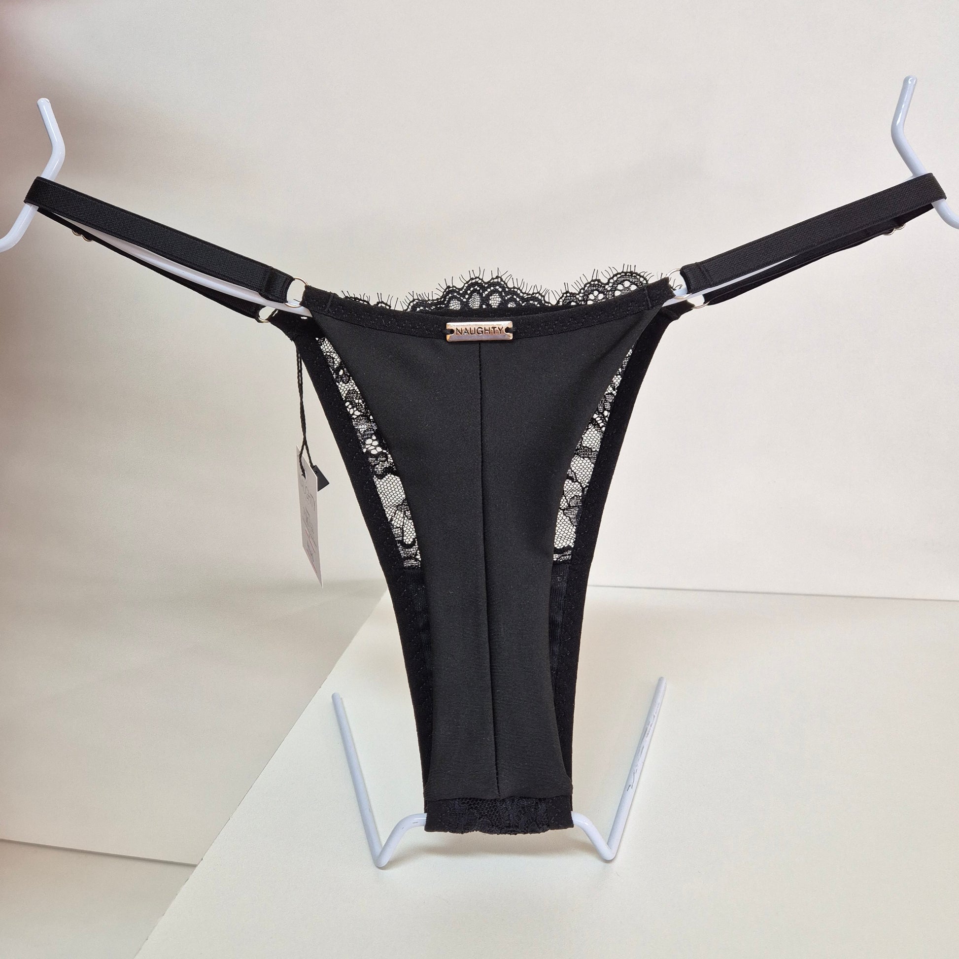 Calcinha string preta em renda macia e floral com alças finas ajustáveis e toque artesanal. Fio duplo em microfibra e plaquinha personalizada naughty na cor prata. 