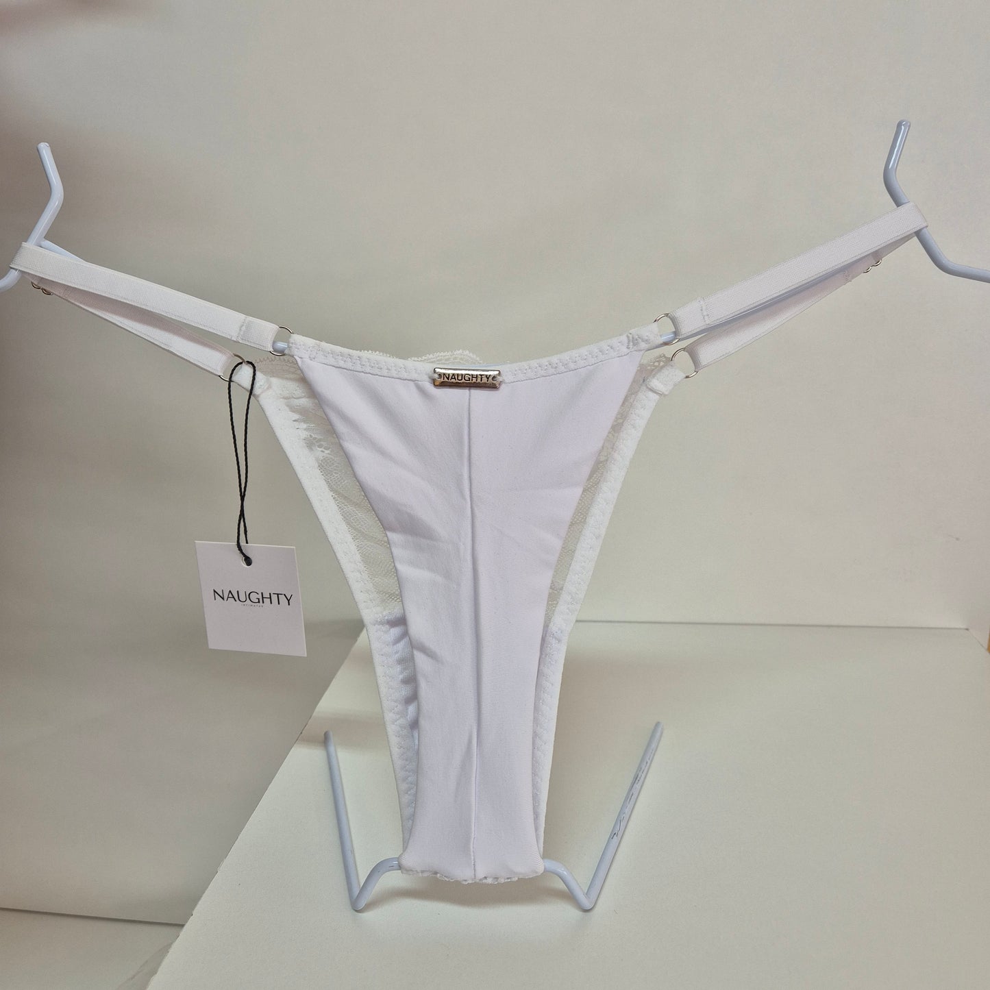 Calcinha string branca em renda macia e floral com alças finas ajustáveis e toque artesanal. Fio duplo em microfibra e plaquinha personalizada naughty na cor prata. 