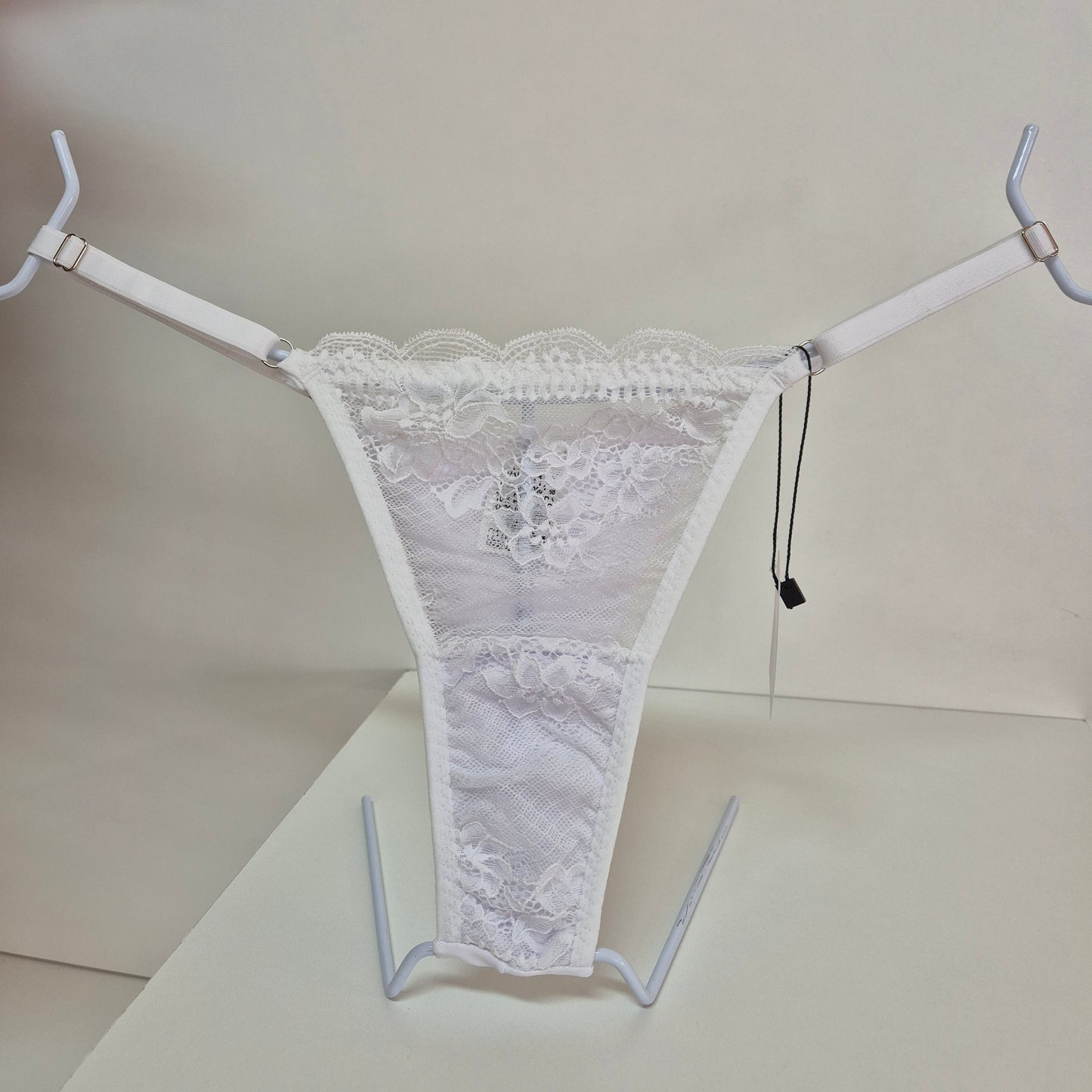 Calcinha string branco em renda macia e floral com alças finas ajustáveis e toque artesanal. Fio duplo em microfibra e plaquinha personalizada naughty na cor prata. 