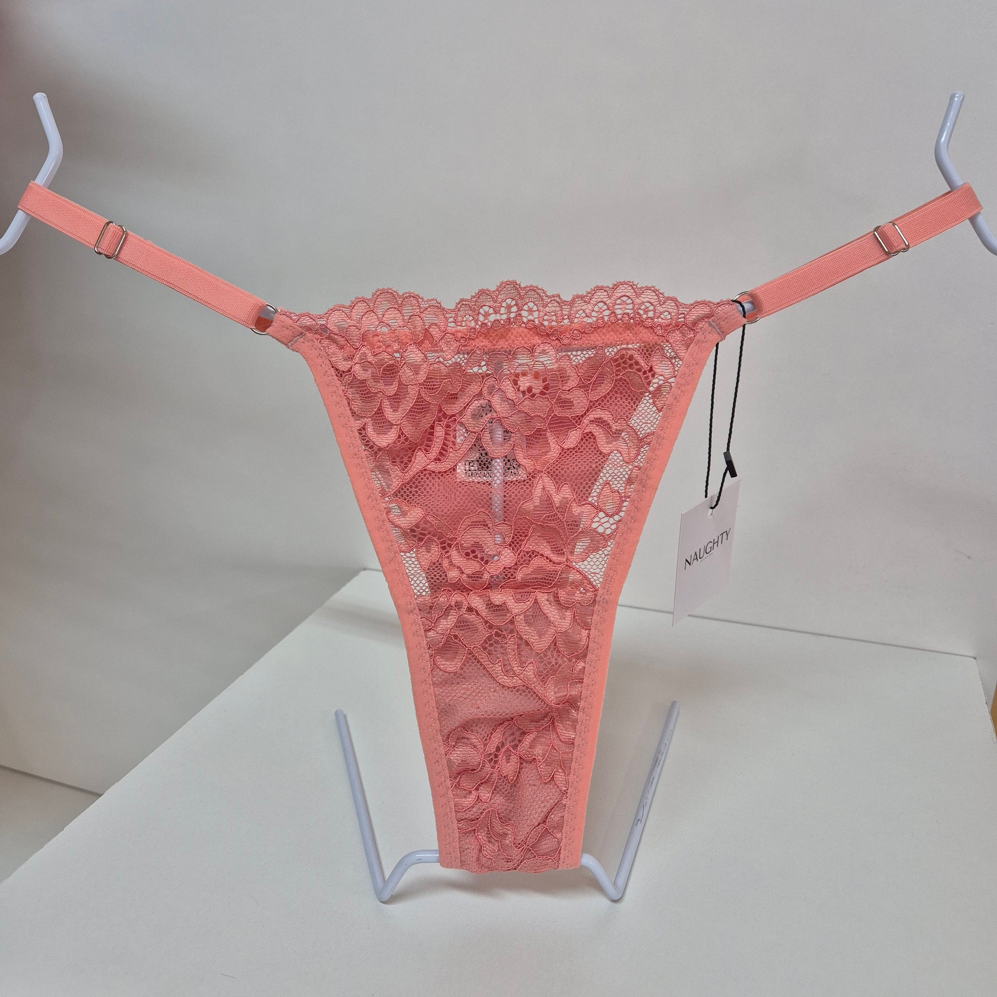 Calcinha string coral em renda macia e floral com alças finas ajustáveis e toque artesanal. Fio duplo em microfibra e plaquinha personalizada naughty na cor prata. 